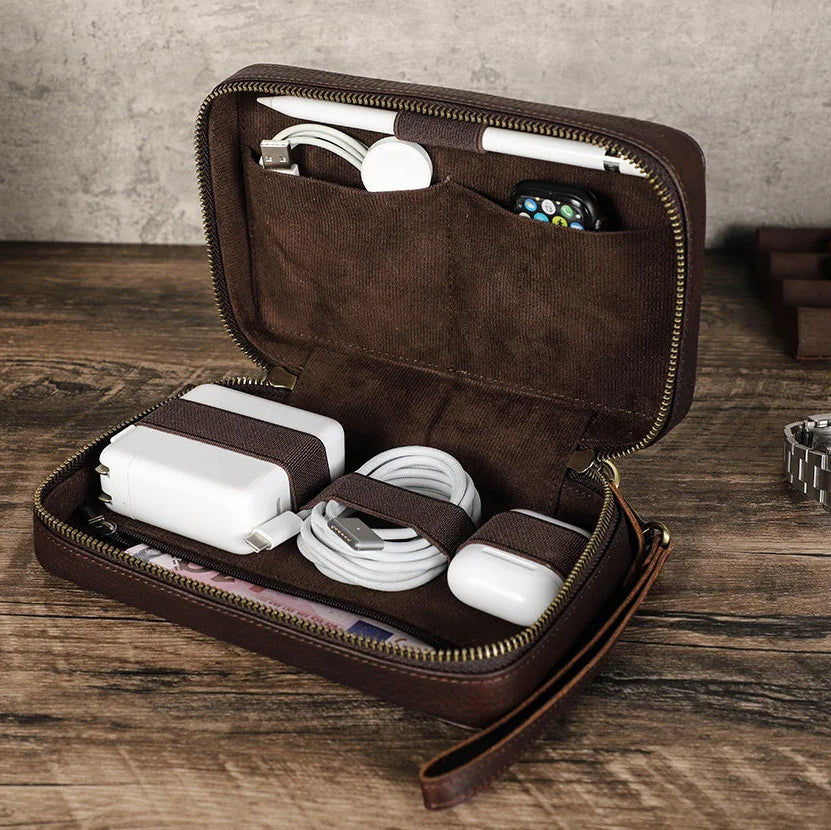 Brown leather travel case with electronic accessories on a wooden surface